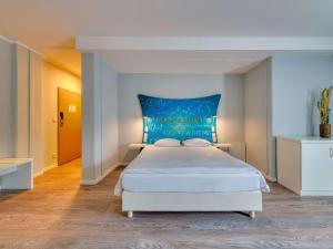 Schlafzimmer mit einem großen weißen Bett mit blauem Kopfteil in der Unterkunft Ibis Styles Regensburg in Regensburg