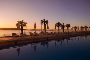 a group of chairs and palm trees next to a pool at DoubleTree by Hilton Malta in St Paul's Bay