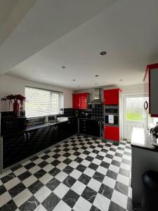 kuchnia z czerwonymi szafkami i czarno-białą podłogą wyłożoną szachownicą w obiekcie Spacious 3-Bed Haven - Free Parking & Wi-Fi w mieście Whitefield