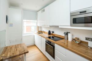 a kitchen with white cabinets and a wooden counter top at Elegant 1BR Apartment Near Central London in London