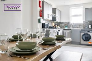 a kitchen with a wooden table with plates and wine glasses at Well-Equipped Serviced Apartments in Aldershot Town Centre, Free WiFi By Redwood Stays in Aldershot