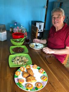 Dua Putri Komodo Homestay في Komodo: رجل كبير في السن يجلس على طاولة مع أطباق من الطعام