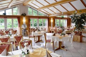 un restaurante con mesas y sillas blancas y ventanas en Hotel Gasthof Am Forsthof, en Sulzbach-Rosenberg