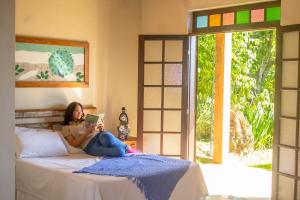 a woman sitting on a bed reading a book at Vila Chico in São Lourenço