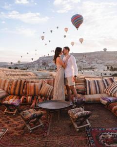 un hombre y una mujer de pie junto a una mesa con globos de aire caliente en Perla Cappadocia en Göreme