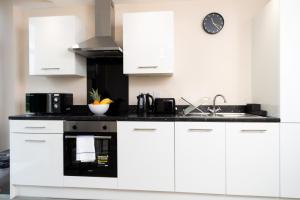a kitchen with white cabinets and a sink and a clock at Stylish Living: 1BR Apt near MCR Central in Manchester