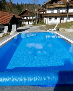 une grande piscine bleue avec des chaises et une maison dans l'établissement Wohnung in Hauzenberg mit Terrasse, gemeinsamem Pool und Garten, à Hauzenberg