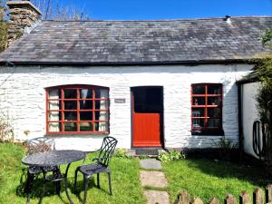 a white house with a red door and a table at Y Beudy Llangrannog in Llangranog