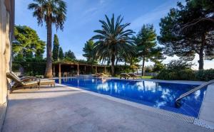 a swimming pool with chairs and palm trees at Villa Meje Split heated pool, jacuzzi, sauna in Split
