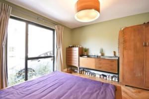 um quarto com uma cama roxa e uma grande janela em Modern 2 bed flat with gardens em Londres