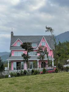 uma casa cor-de-rosa com uma cerca branca num campo em Lucia Villa - Melorita Hòa Lạc em Hanói