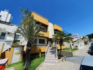 un edificio amarillo con palmeras delante en Acapulco - Apartamentos em Bombinhas, en Bombinhas