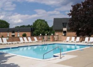 uma grande piscina com cadeiras brancas e um edifício em Two-Bedroom Two-Bathroom Gem Near Downtown Rochester Hills em Rochester Hills