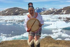 un hombre sosteniendo un tambor delante de una montaña en Hotel Aurora Apartments, en Nuuk