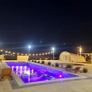 una piscina con luces moradas por la noche en Desert Breeze en Al Ḩamrānīyah