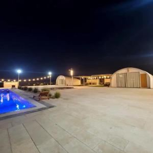 Desert Breeze في Al Ḩamrānīyah: موقف كبير للسيارات مع حمام سباحة في الليل