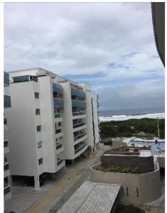 two tall white buildings next to the ocean at Apartamento aconchegante vista mar e piscina em cond de Arraial do Cabo in Arraial do Cabo