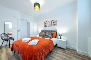 - une chambre dotée d'un lit avec des draps orange et une chaise dans l'établissement Modern 2 bed in Potters Bar - with FREE Parking- 4 min walk from the TRAIN STATION - DIRECT TRAINS TO LONDON, à Potters Bar