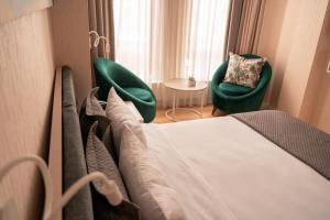 a hotel room with a bed and two green chairs at Hotel Well Inn in Tbilisi City