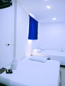 two white beds in a room with a blue light at Hostal Martha in Neiva