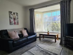 uma sala de estar com um sofá de couro preto e uma televisão em Blodfa em Holyhead