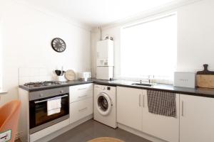 a kitchen with white cabinets and a washer and dryer at Liverpool Haven: Charming Private Room in Liverpool
