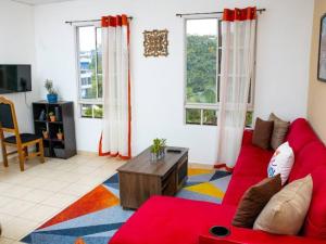 a living room with a red couch and two windows at Cozy Two Bedroom Apartment Near The U.S. Embassy in Antiguo Cuscatlán