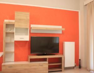 a living room with an orange wall with a flat screen tv at Άνετο και όμορφο διαμέρισμα in Xanthi