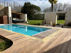 a swimming pool with a wooden deck next to a house at Domaine de la Gémolière in Gémozac