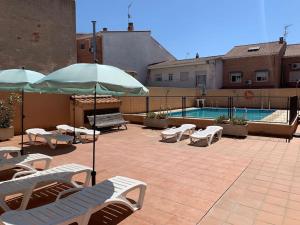 eine Terrasse mit Stühlen und Sonnenschirmen neben einem Pool in der Unterkunft apartamento familiar con piscina in Camarma de Esteruelas