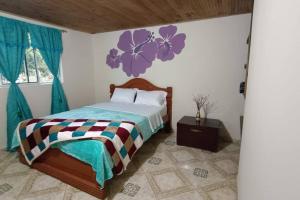 1 dormitorio con 1 cama con flores púrpuras en la pared en Casa Rio de Cristal en Pijao