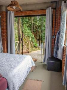 Schlafzimmer mit einem Bett und einer Glasschiebetür in der Unterkunft Suíte com cachoeira no quintal in Antônio Carlos