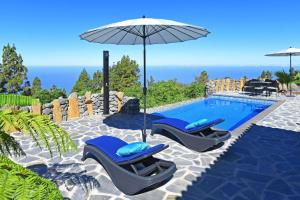 een zwembad met twee blauwe stoelen en een parasol bij Ferienhaus mit Privatpool für 4 Personen ca 85 qm in Tijarafe, La Palma Westküste von La Palma in Tijarafe