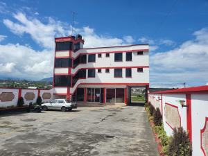 un bâtiment blanc avec une voiture garée dans un parking dans l'établissement Hostal La Cocha, à Latacunga