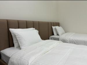 two beds with white pillows in a room at MFAPARTMENT in Al Budayyiâ€˜