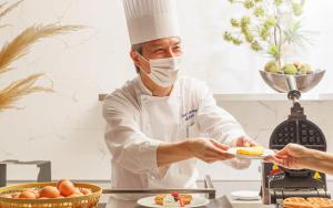 a chef wearing a mask holding a plate of food at Hotel Monterey Himeji in Himeji