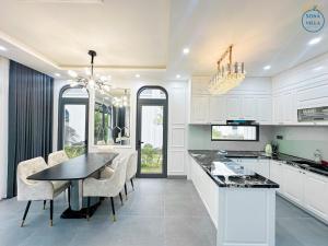 a kitchen with white cabinets and a table and chairs at Royal Beach Villa Sonasea Vân Đồn Quảng Ninh 