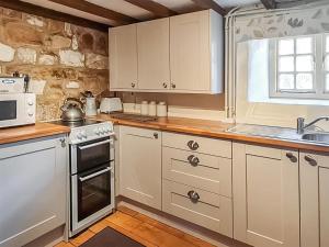 eine Küche mit weißen Schränken und einem Herd mit Backofen in der Unterkunft Nightingale Cottage - Ukc1570 in Crich
