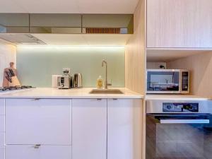 La cuisine est équipée de placards blancs et d'un four micro-ondes. dans l'établissement City Living Made Easy : 1 Bed Apt in Ashfield Heart, à Sydney
