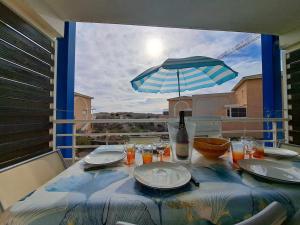 una mesa con platos y una sombrilla en el balcón en Appartement Marseillan-Plage, 2 pièces, 6 personnes - FR-1-326-816, en Marseillan