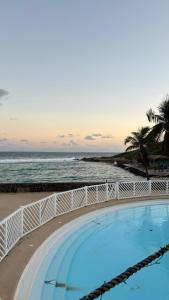 ein Pool neben einem Strand mit dem Meer in der Unterkunft Good Mood Studio - Manganao Hôtel in Saint-François