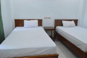 two beds in a room with white sheets at Mahoni Guest House Labuan Bajo in Labuan Bajo