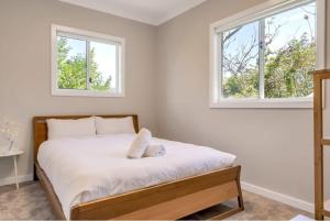 Cosy & Modern Mountain Getaway Katoomba في كاتومبا: غرفة نوم بيضاء مع سرير مع نافذتين