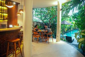 two people sitting at a table in a restaurant with a pool at djabu Seminyak Hotel in Seminyak