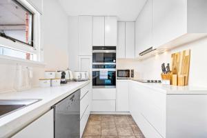 uma cozinha branca com armários e electrodomésticos brancos em Vivid Sydney Landmark Views from Luxury 2Bd Apt em Sydney
