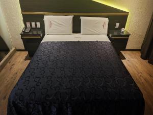 a bedroom with a bed with a black blanket and white pillows at Hotel Dubái in Texcoco de Mora