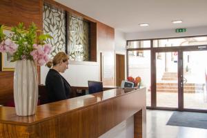 Eine Frau, die an einem Schreibtisch mit einer Blumenvase sitzt. in der Unterkunft Hotel BELASSI in Bojnice