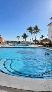 une grande piscine avec des palmiers et l'océan dans l'établissement Quintas del mar Mazatlán, à Mazatlán