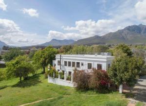 a white house on a hill with mountains in the background at Boord Guest House in Stellenbosch