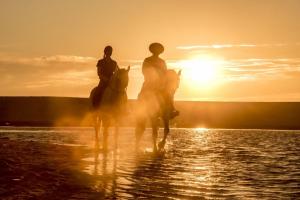 dos personas montando caballos en el agua al atardecer en Casa Sol e Areia Villa Eira Nova en Porto Covo
